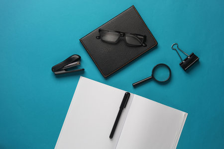 Blank open notebook and office stationery on blue background. Flat lay