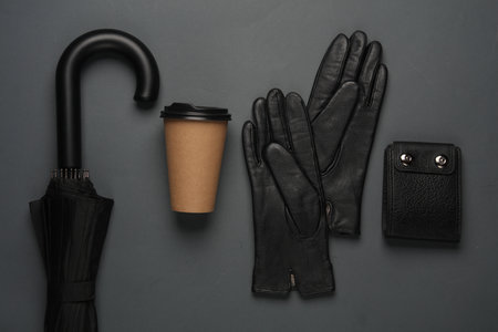 Black umbrella with leather gloves, purse and coffee cup on a dark backgroundの写真素材