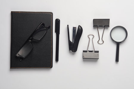 Notebook, stapler, eyeglasses, binders, magnifying glass on white background. Black stationery objects. Top view. Flat layの写真素材