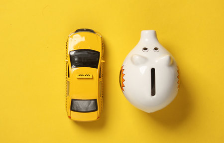 Toy taxi car model with piggy bank on yellow background. Travel concept. Top view