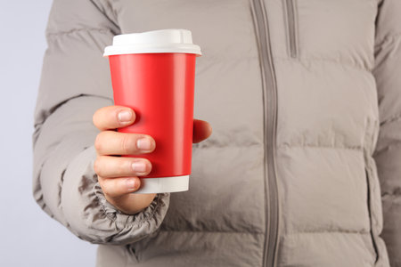 Man in a down jacket holds paper red coffee cup on a gray backgroundの写真素材