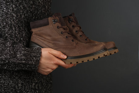 Man in sweater holding leather bootsの写真素材