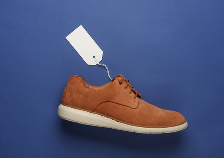 Suede shoe with white blank tag on string, blue background. Template for design, sale, shopping conceptの写真素材
