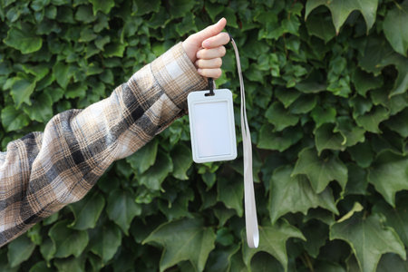 Hand holding id tag on green leaves wall background