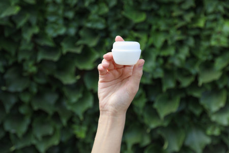 Hand holding white cream jar on green leaves wall backgroundの写真素材