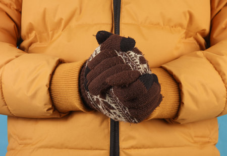 Man in yellow winter down jacket and gloves on blue background