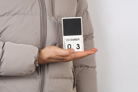 Man in down jacket holds wooden block calendar with date December 1