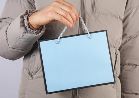 Man's hand in down jacket holding paper bagの写真素材