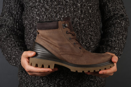 Man in sweater holding leather bootsの写真素材
