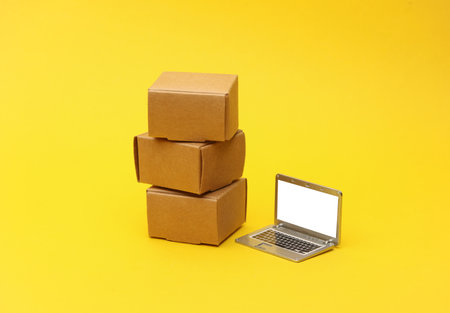 Miniature Boxes and laptop on a yellow background. Logistics, transportation, delivery
