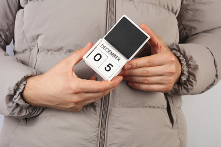 Man in down jacket holds wooden block calendar with date December 5