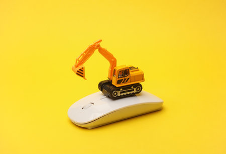 Toy excavator and pc mouse on yellow background