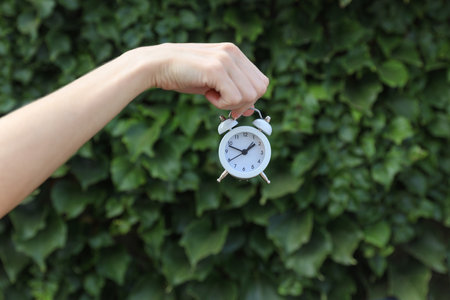 Alarm clock in hand on green leaves wall background