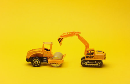 Toy asphalt paver and excavator on yellow backgroundの写真素材