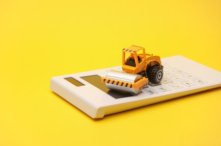 Toy asphalt paver and calculator on yellow background