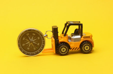 Miniature toy forklift and compass on a yellow background. Logistics, transportation, deliveryの写真素材