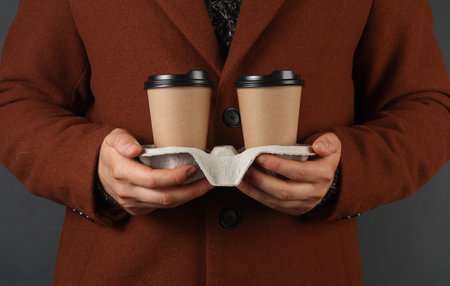 Man in woolen coat holds coffee cups in tray on dark gray backgroundの写真素材