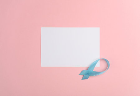 White blank sheet of paper and blue awareness ribbon on pink backgroundの写真素材