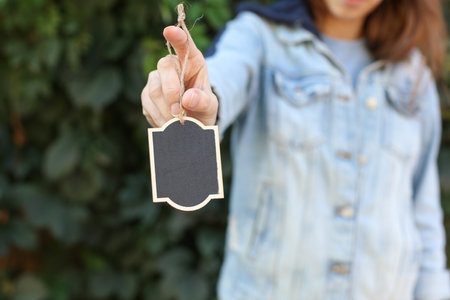 Hand holding Chalkboard label, blank wooden blackboard tag, garden sign on green leaves wall backgroundの写真素材