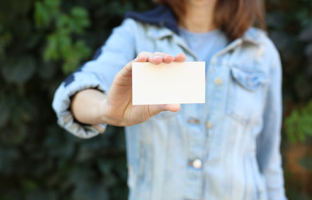 Woman in jeans jacket holding business card against green plants wall backgroundの写真素材