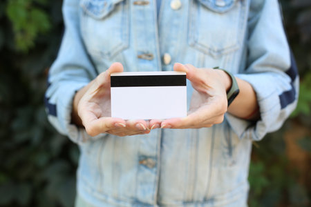 Woman in jeans jacket holding credit card against green plants wall backgroundの写真素材