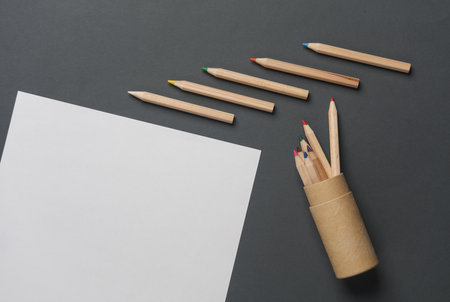 Box with wooden colored pencils and paper sheet on dark gray background. Creativity, art. Top view