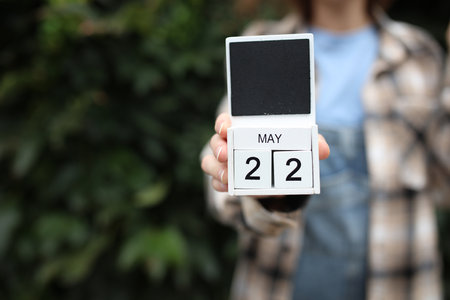Woman holds calendar with the date May 22 outdoors.
