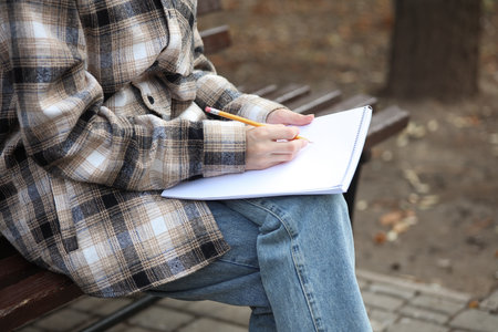Woman in a warm shirt with sketchbook and pencil on a bench in an autumn parkの写真素材
