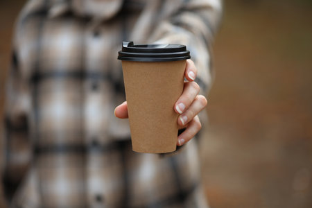 Woman in warm shirt holds cardboard cup for hot drink (coffee, cup) outdoors in autumn parkの写真素材