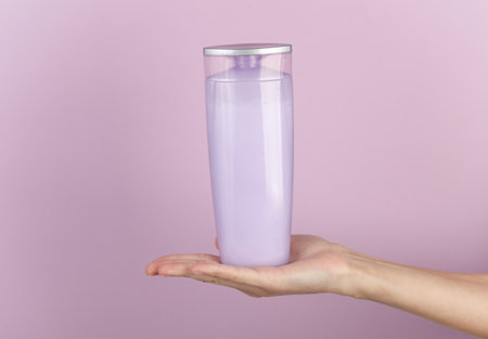 Female hand holding bottle of shampoo on purple pastel backgroundの写真素材