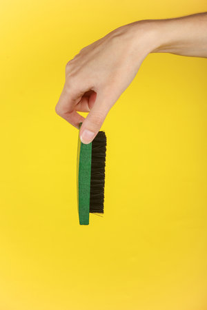 Woman's hand holding a shoe brush on a yellow backgroundの写真素材