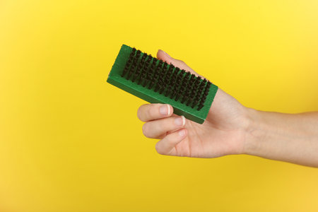 Woman's hand holding a shoe brush on a yellow backgroundの写真素材