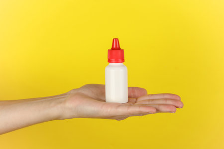 Hand holding white bottle of shoe polish on yellow backgroundの写真素材