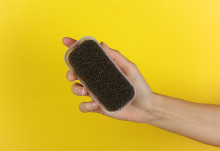 Hand holding a sponge for cleaning suede shoes on a yellow background