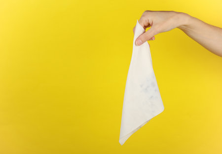 Hand holding a white rag or cloth wipe on a yellow backgroundの写真素材