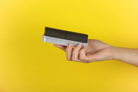 Hand holding a sponge for cleaning suede shoes on a yellow backgroundの写真素材