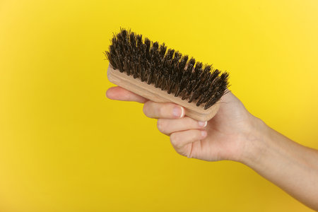 Woman's hand holding a shoe brush on a yellow backgroundの写真素材