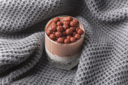 Homemade layered Dessert in a glass cup with yogurt and chocolate balls on gray fabric blanketの写真素材