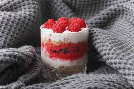 Homemade layered Dessert in a glass cup with yogurt and raspberries on gray fabric blanketの写真素材