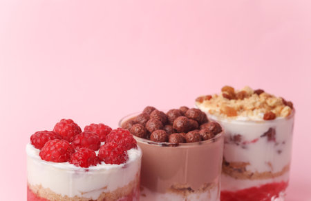 Homemade layered Desserts in a glass cups with yogurt, berries and chocolate on a pink backgroundの写真素材