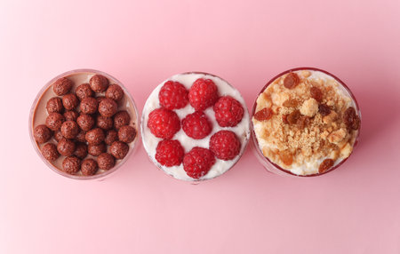 Homemade layered Desserts in a glass cups with yogurt, berries, cookies and chocolate on a pink background. Top viewの写真素材