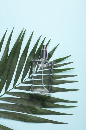 Perfume bottle with green palm leaf on blue background. Creative layout of beauty and fashion still...