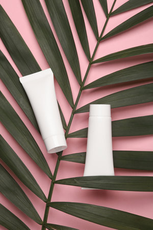 White cream tubes with green palm leaf on pink background. Creative layout of beauty and fashion still lifeの写真素材