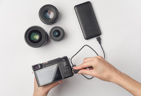 Hands holding modern camera charged from external power bank battery on white background