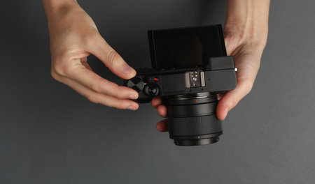 Hands holding modern mirrorless camera on dark gray background