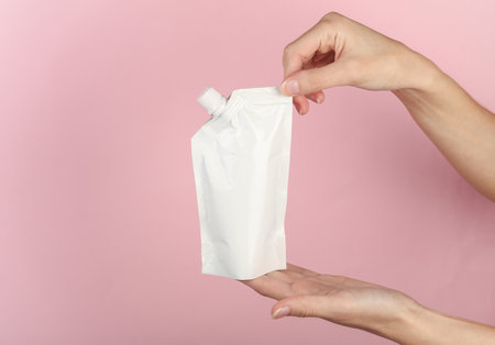 Hands holding white doy pack with dispenser on a pink background. Template for design, mockup