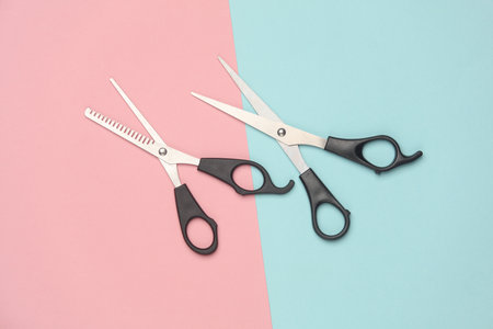 Two pairs of haircutting scissors on a pink blue background