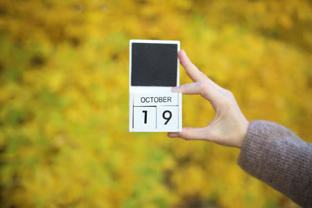 Woman holding calendar with date October 19 on yellow autumn leaves backgroundの写真素材