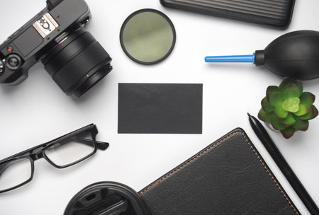 Black business card on a white background with a camera, notepad and modern accessories and gadgets...