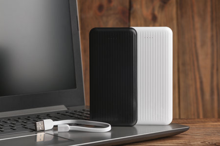Laptop with power banks external battery on wooden background
